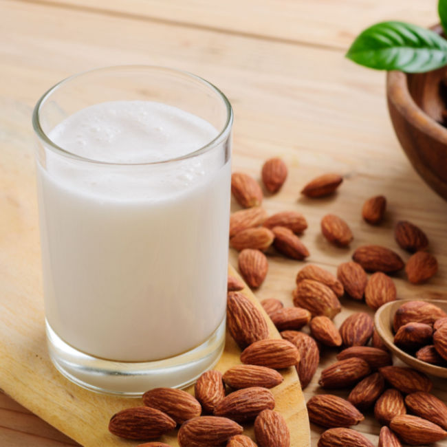 glass of almond milk surrounded by almonds