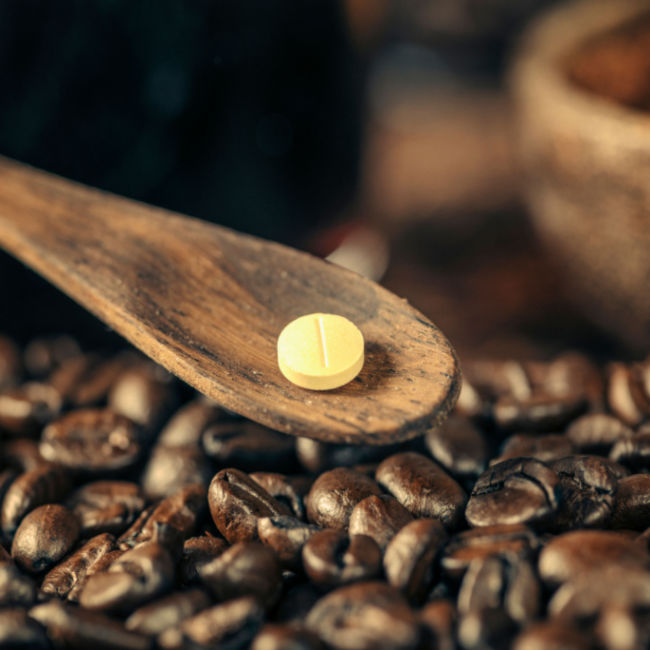 caffeine pill on spoon top of coffee beans