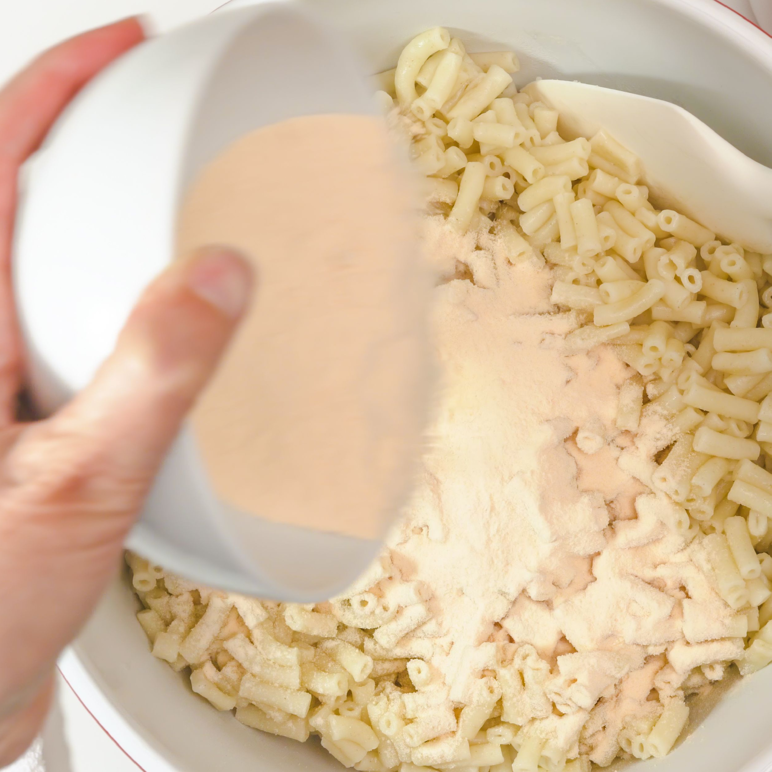 person adding cheese powder to macaroni