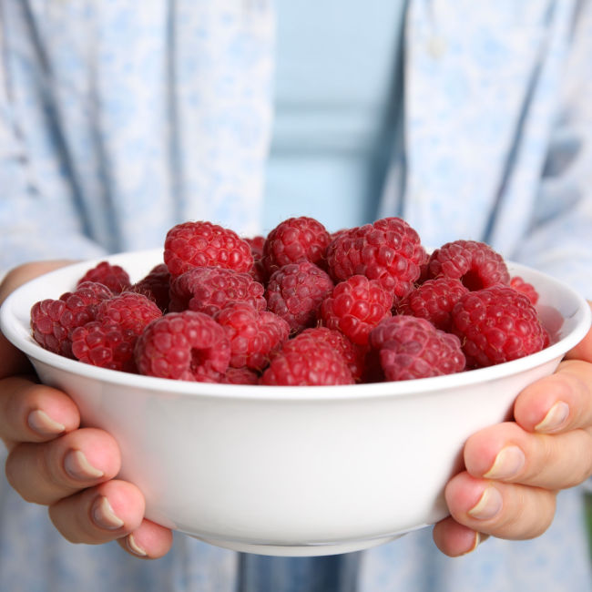 person holding bowl of raspberries