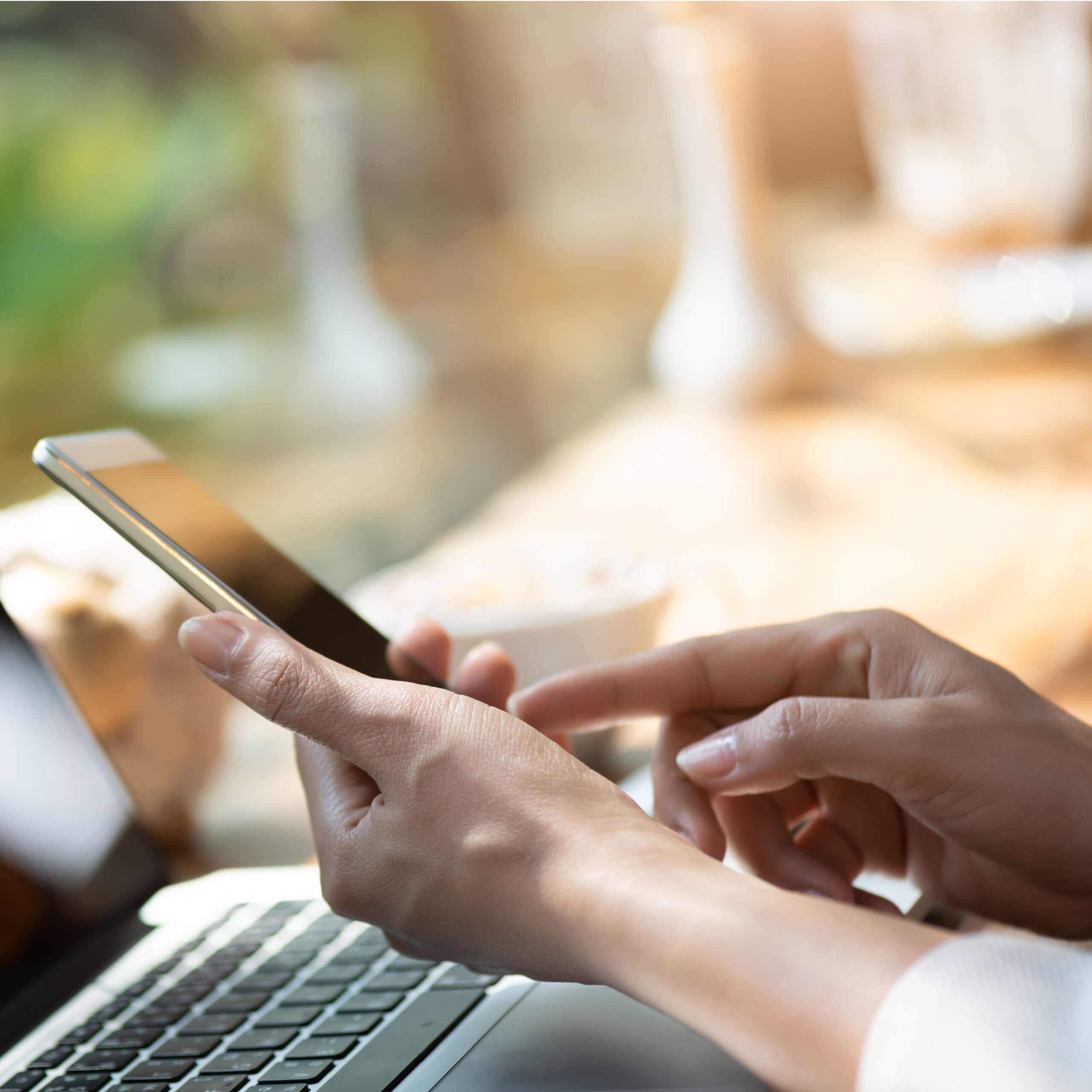 person holding phone at laptop