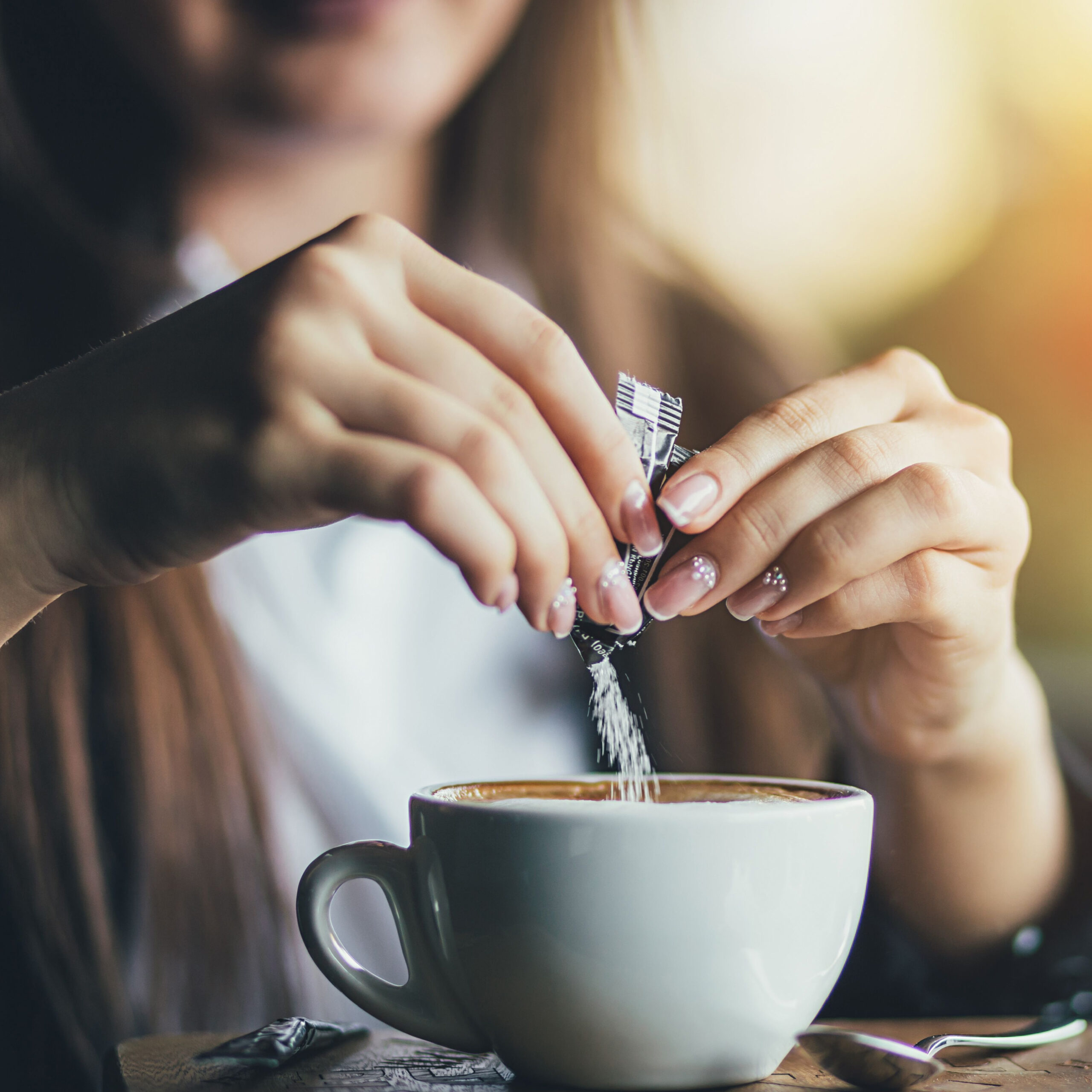 woman adding sugar to cup of coffee