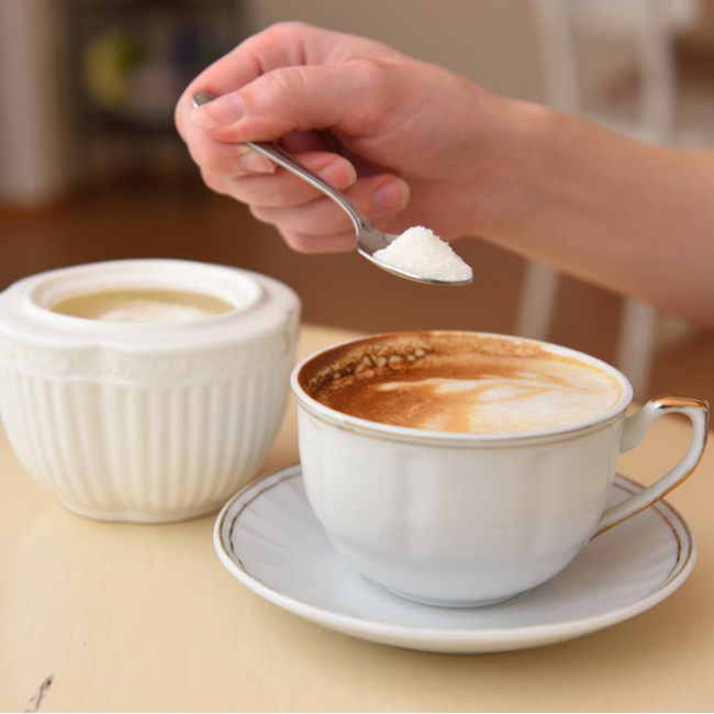 person adding sugar to coffee