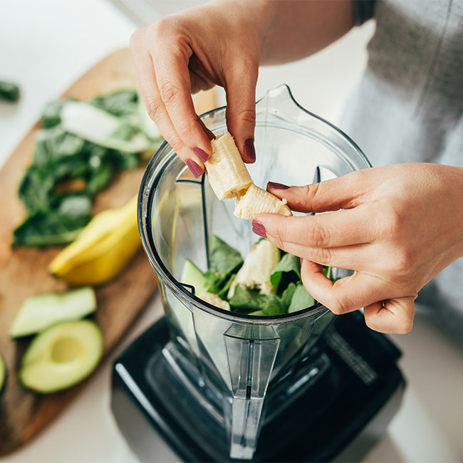 woman adding smoothie ingredients to blender