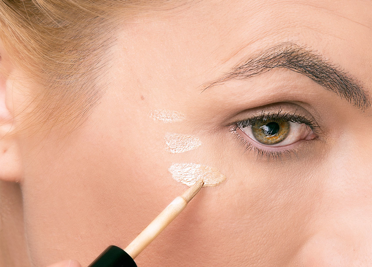 woman applying concealer to under eye