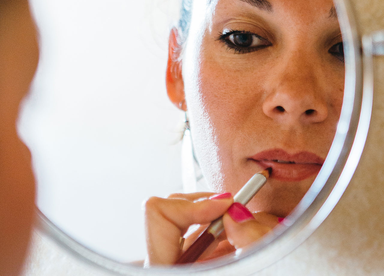 woman looks in the mirror applying lip liner