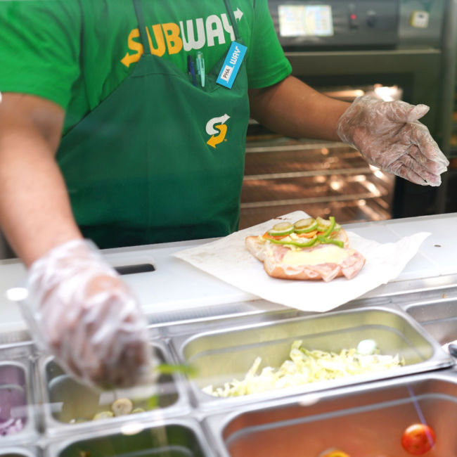 subway sandwich artist making sandwich at counter