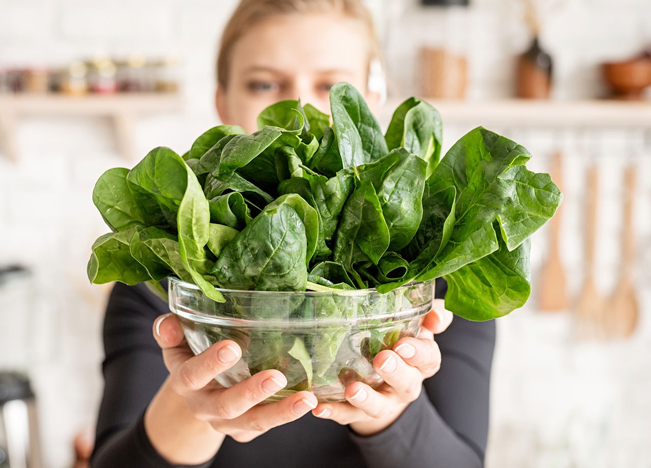 woman holding up a bowl of spinach