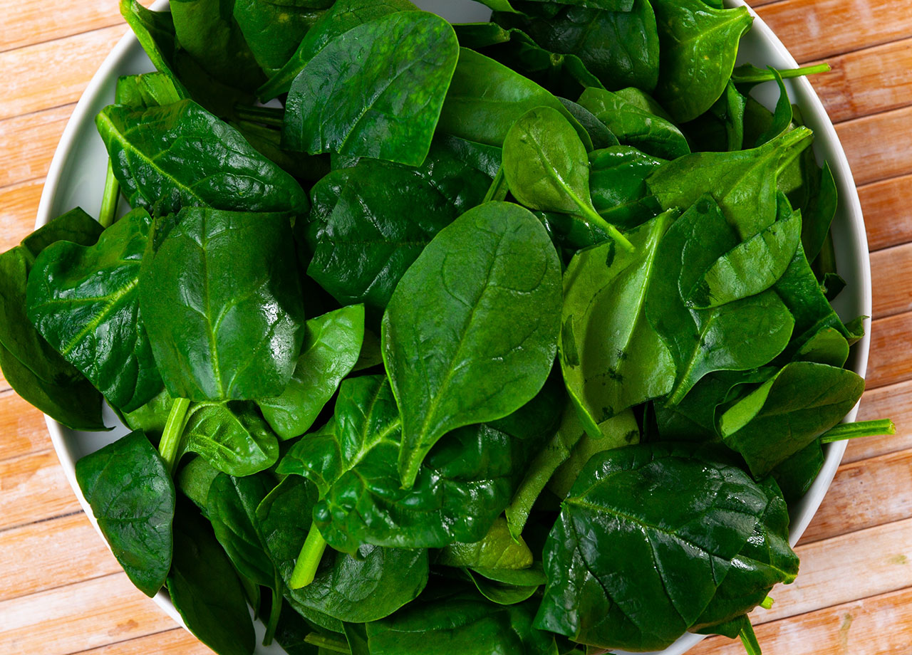 fresh green spinach leaves on wooden table and in a bowl