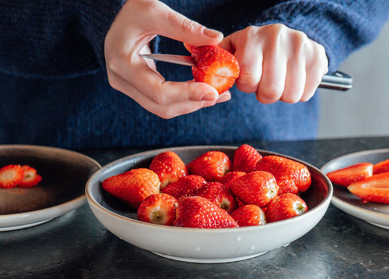 hands cut fresh strawberries and put in a plate