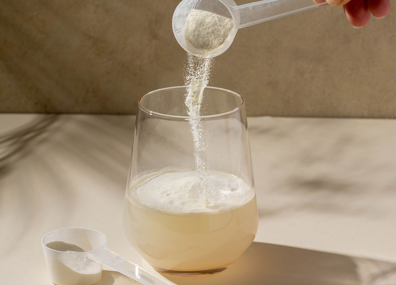 collagen protein powder added with measuring scoop in a glass of water