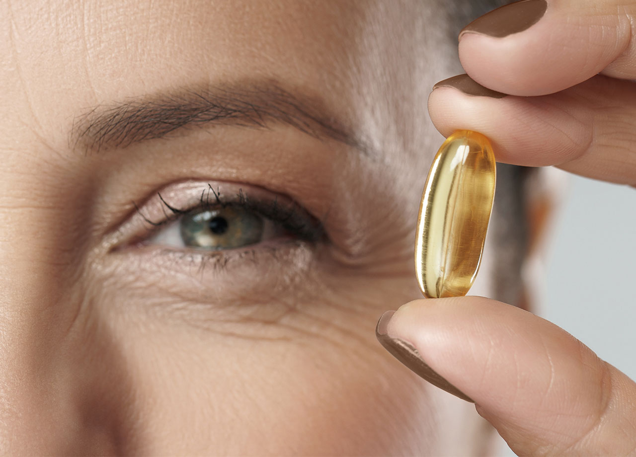 aged woman holds up omega 3 fatty acids pill