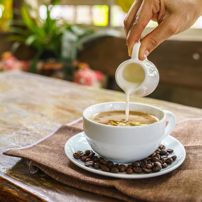 woman adding cream to coffee