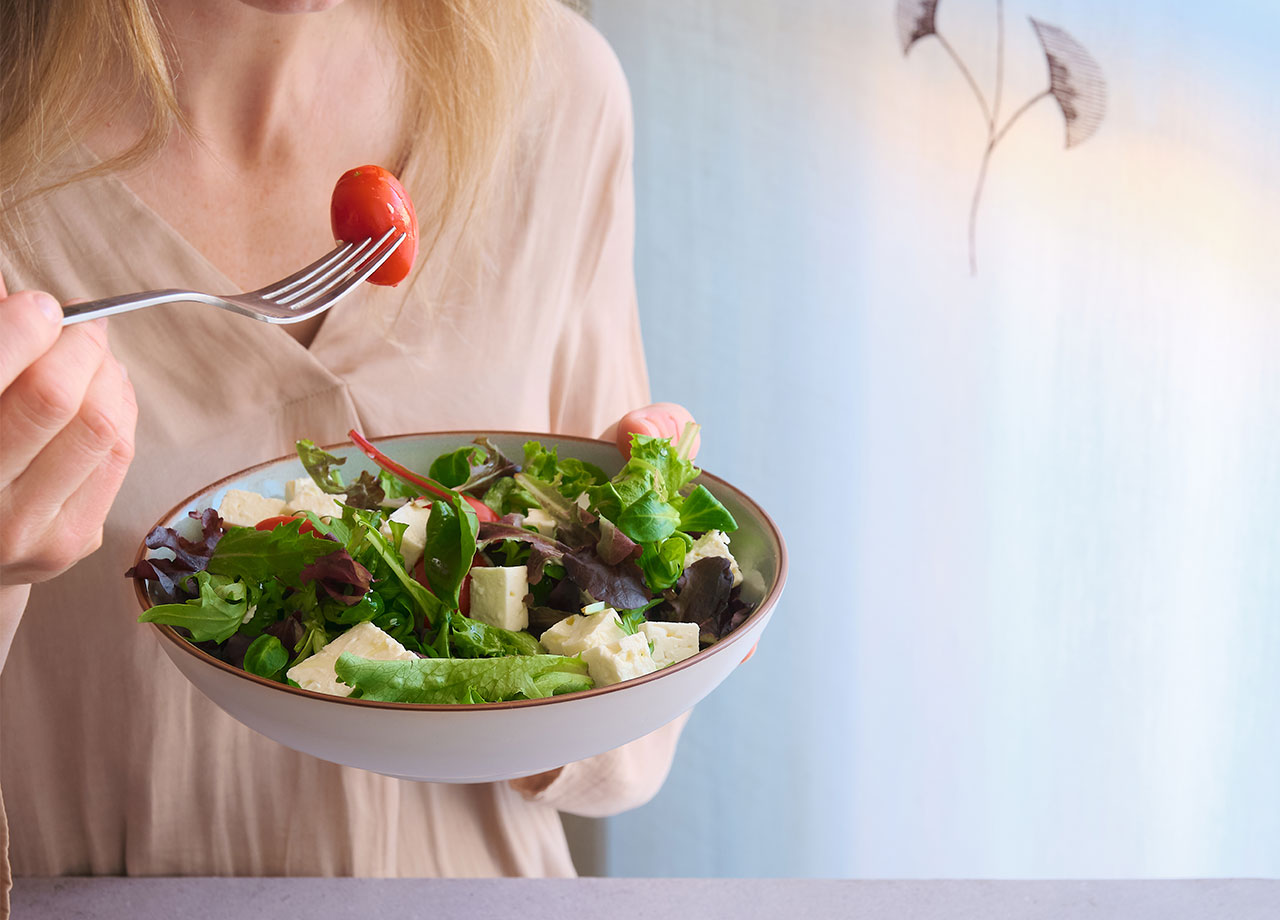 "Fit woman eating avocado, cucumber, and tomatoes"