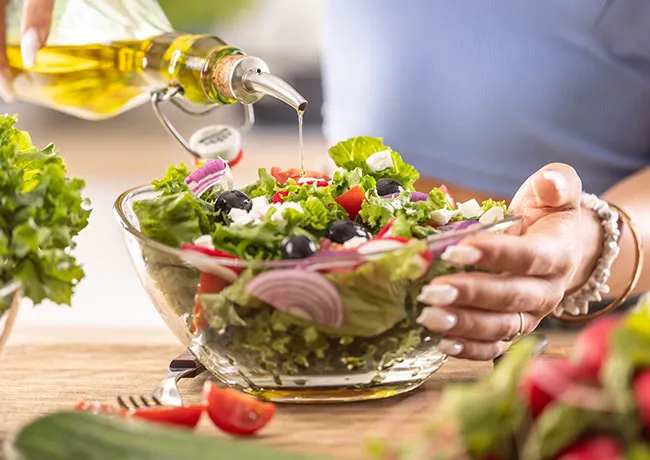 woman pouring olive oil onto salad