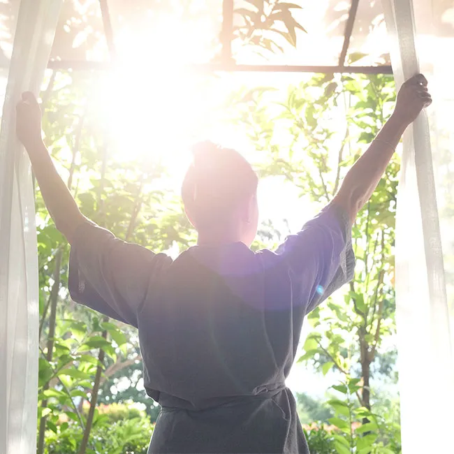 "Woman opening curtains for morning sunlight"