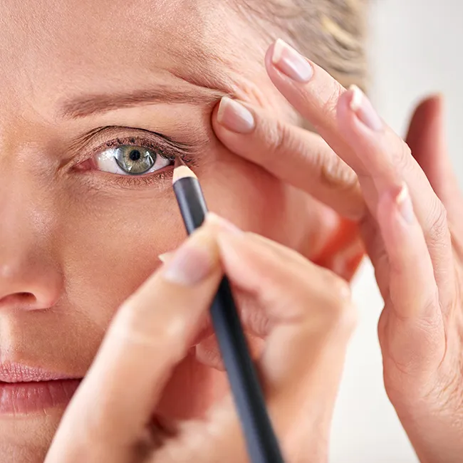 Middle-aged woman applying eyeliner in front of a mirror.