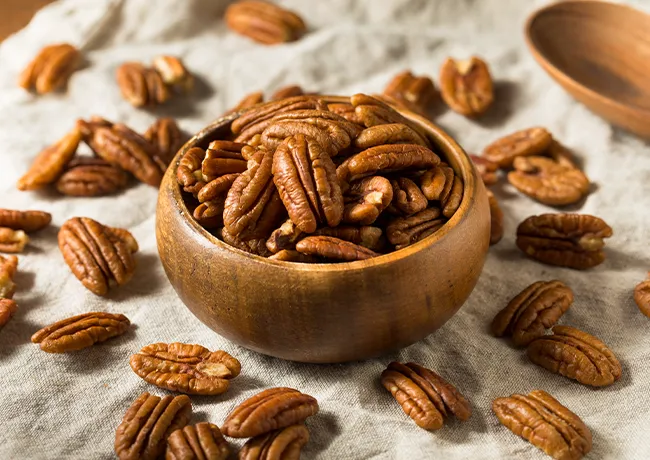"Pecans in a bowl and scattered on a table"
