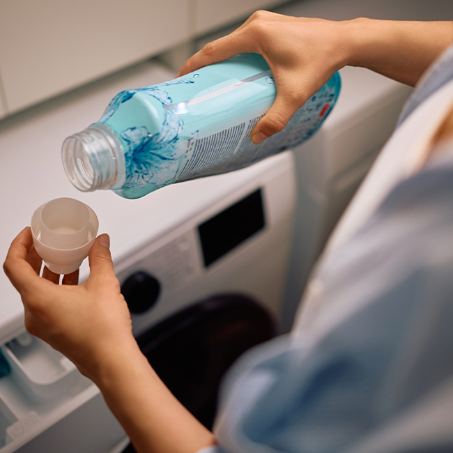 "Woman using fabric softener while doing laundry at home"