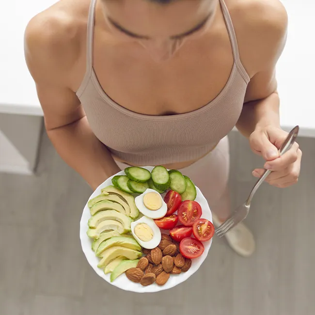 "Fit woman eating avocado, cucumber, tomatoes, and walnuts"