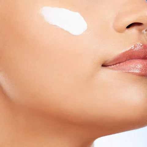 "Woman applying moisturizer on her cheek"